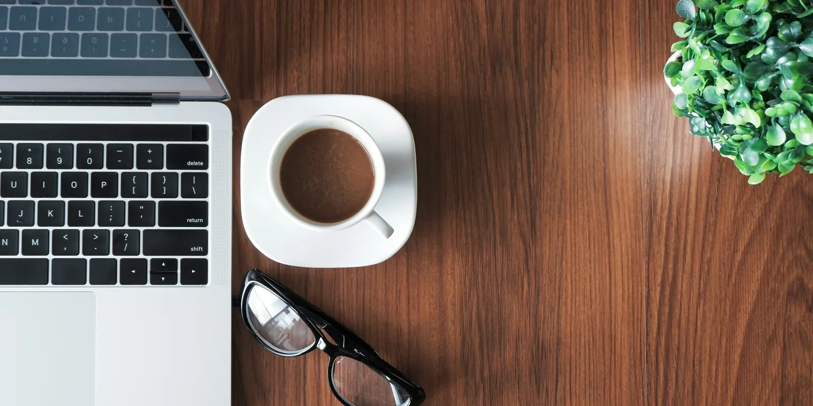 A founder's wooden desk with a laptop, a cup of coffee and a green plant